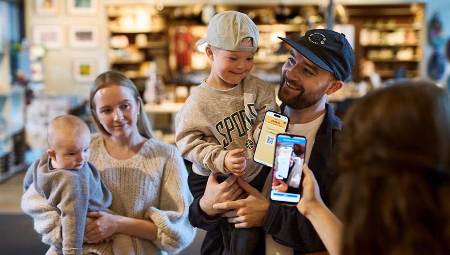 Mother and father each carrying a child and showing the Oslo Pass app to a museum staff member behind a counter.