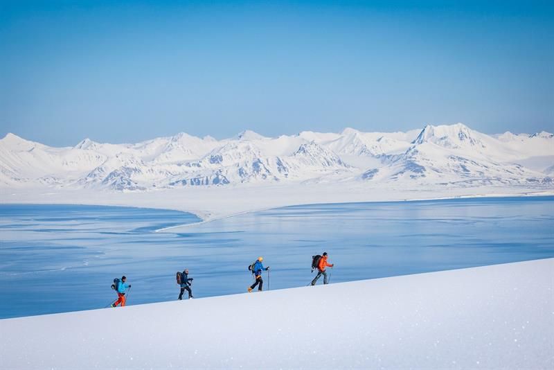 Fire personer går på ski opp et fjell med fjorden og fjell i bakgrunnen.