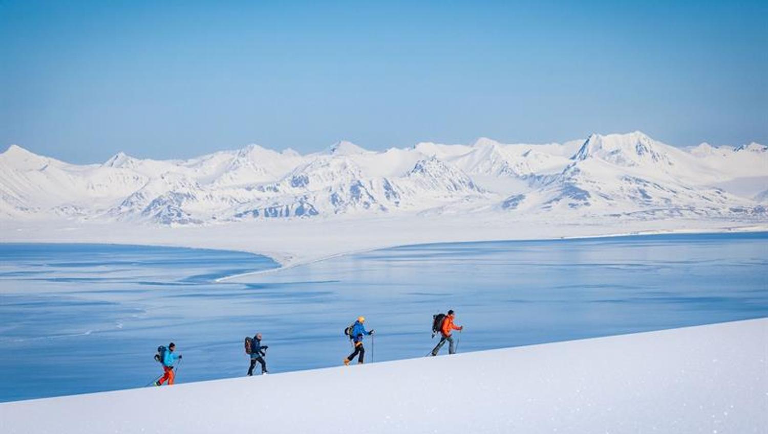 Fire personer går på ski opp et fjell med fjorden og fjell i bakgrunnen.