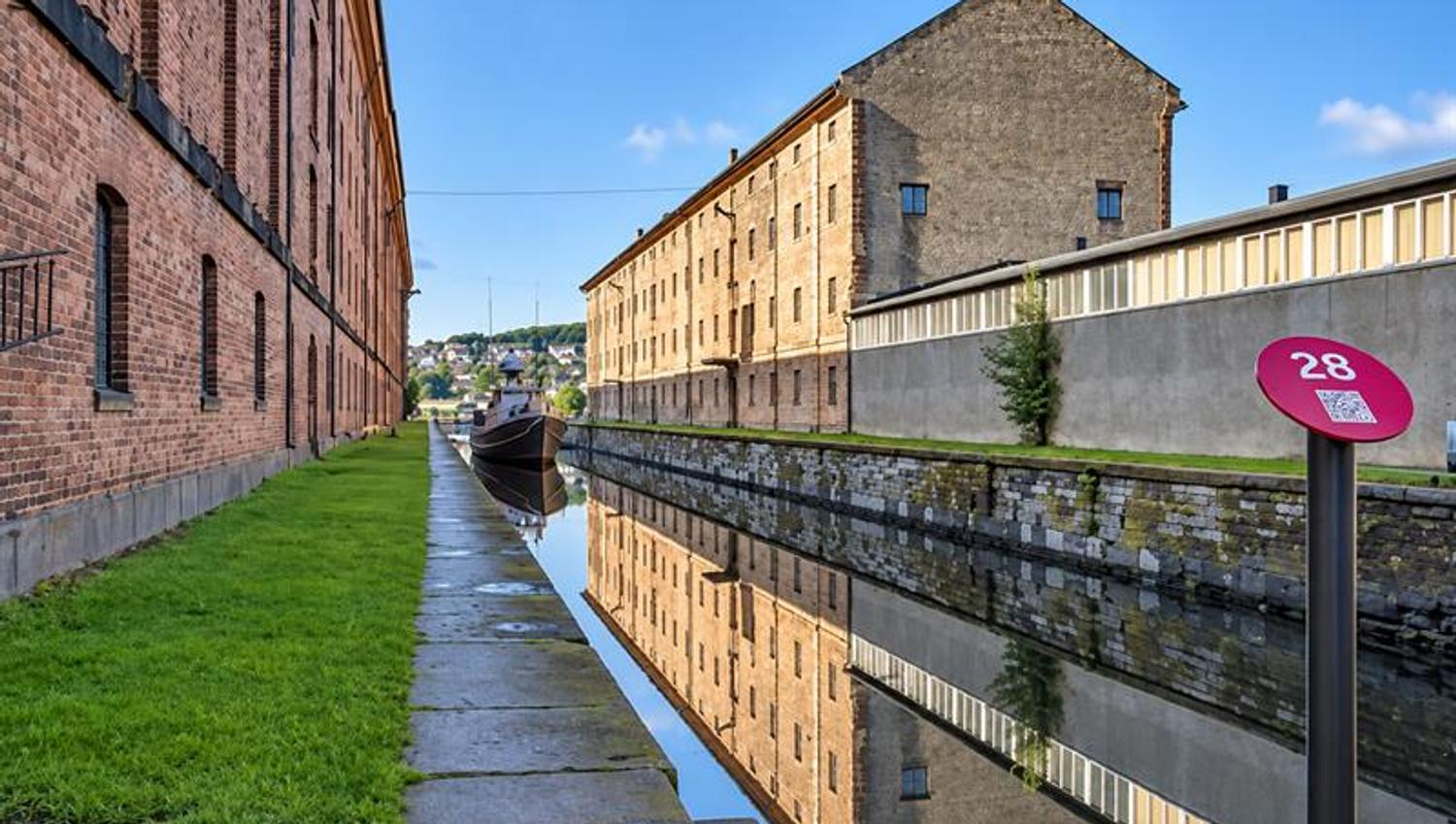 Historiske murbygninger på Karljohansvern i Horten speiler seg i den smale kanalen mellom bygningene.