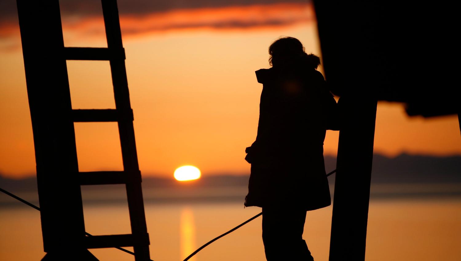 Silhouette of a person looking at the midnight sun