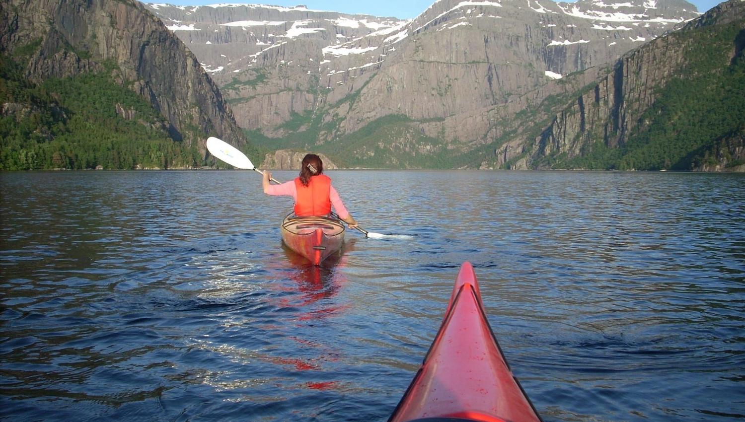 Opplevingar i nærleiken av Bremanger Fjordhotell: Ein person i kajakk padlar på ei stille fjord, med bratte fjell og snøflekker under blå himmel..