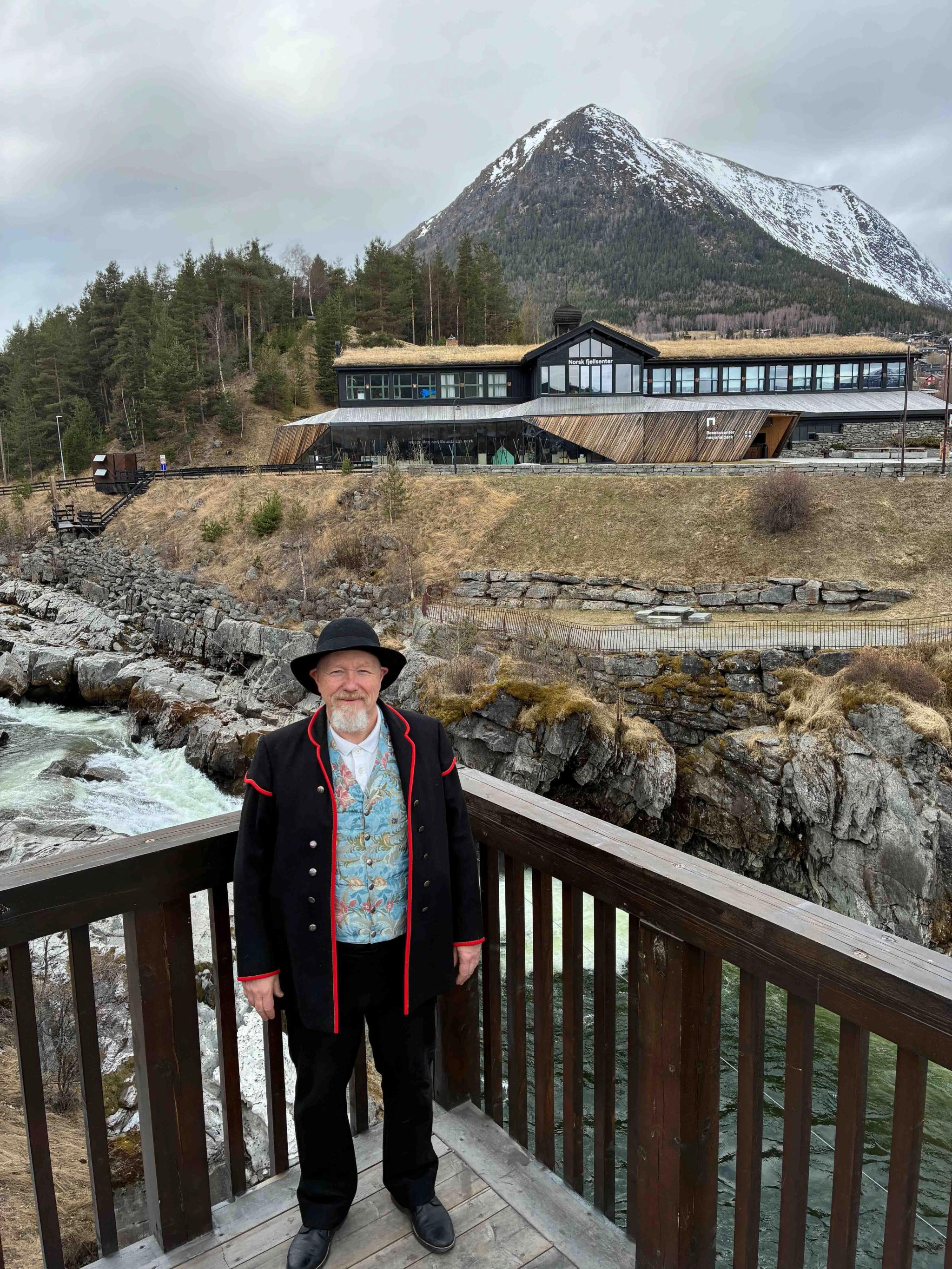 Bjørn Ola Aukrust i bunad på verandaen på bakeriet i Lom. Lomseggen i bakgrunnen. 