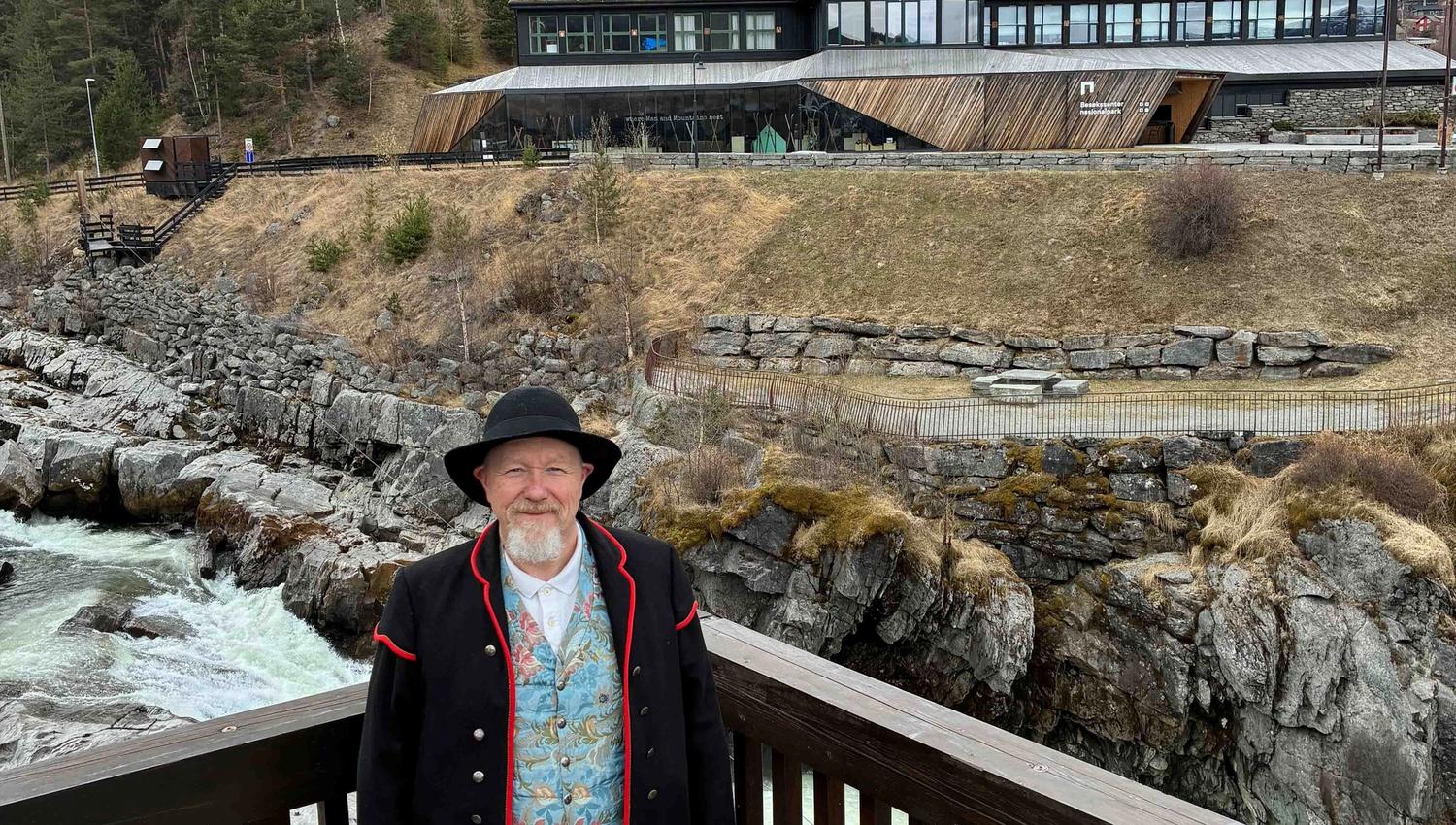 Bjørn Ola Aukrust i bunad på verandaen på bakeriet i Lom. Lomseggen i bakgrunnen.