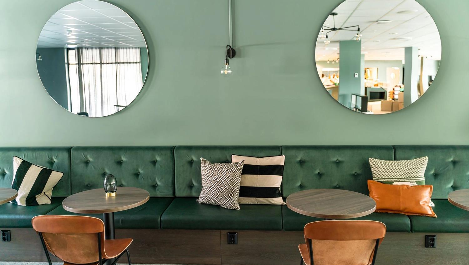 Cozy seating corner with two round mirrors and green sofa cushions.