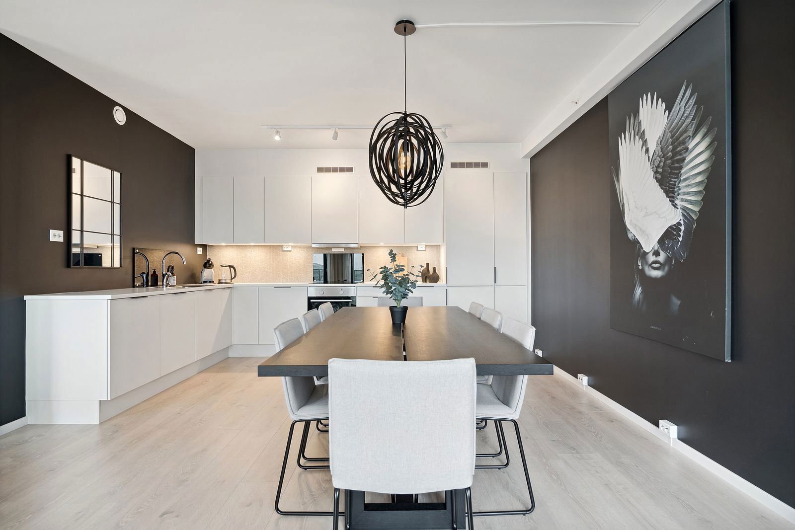 Moderne kjøkken og spisestue med hvite møbler, svarte detaljer og kunst på veggen.