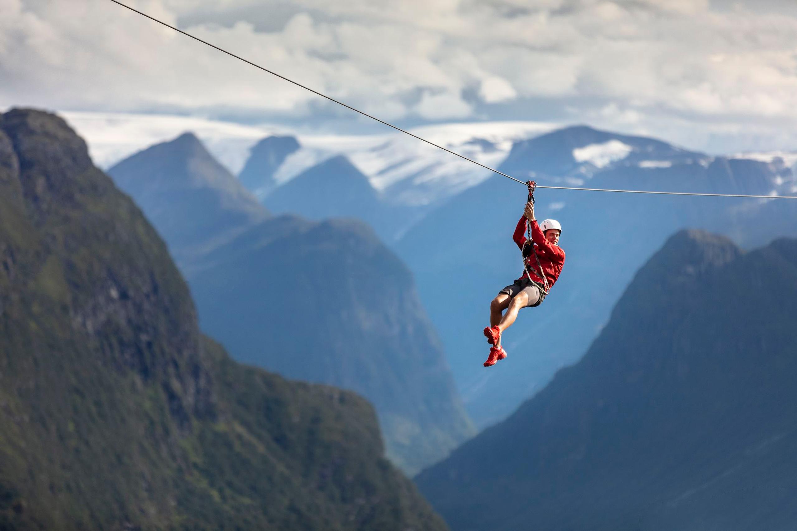 En person suser i zipline over dype fjella i Nordfjord i bakgrunnen