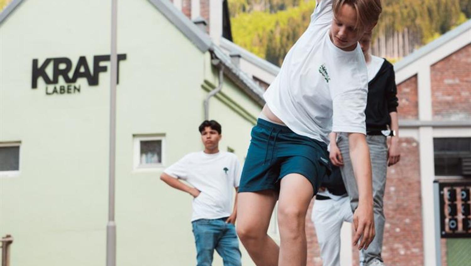 Ungdom utøver skateboard-triks på plassen utanfor KraftLaben i Odda, med Hardanger-fjella som grønt bakteppe.