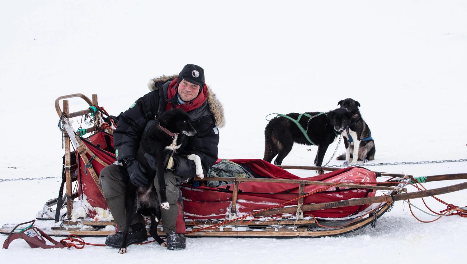 A guide (Tommy Jordbrudal) sitting on a dog sled together with a dog