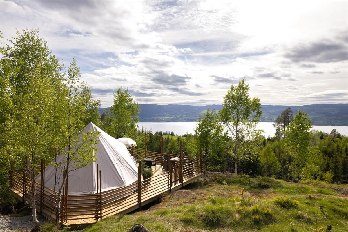 A tent set in green woodland with a view toward a lake.