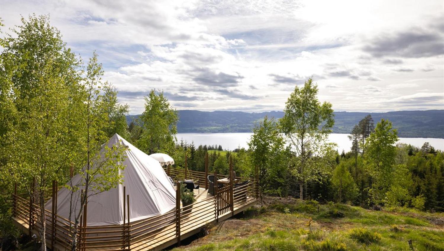 A tent set in green woodland with a view toward a lake.