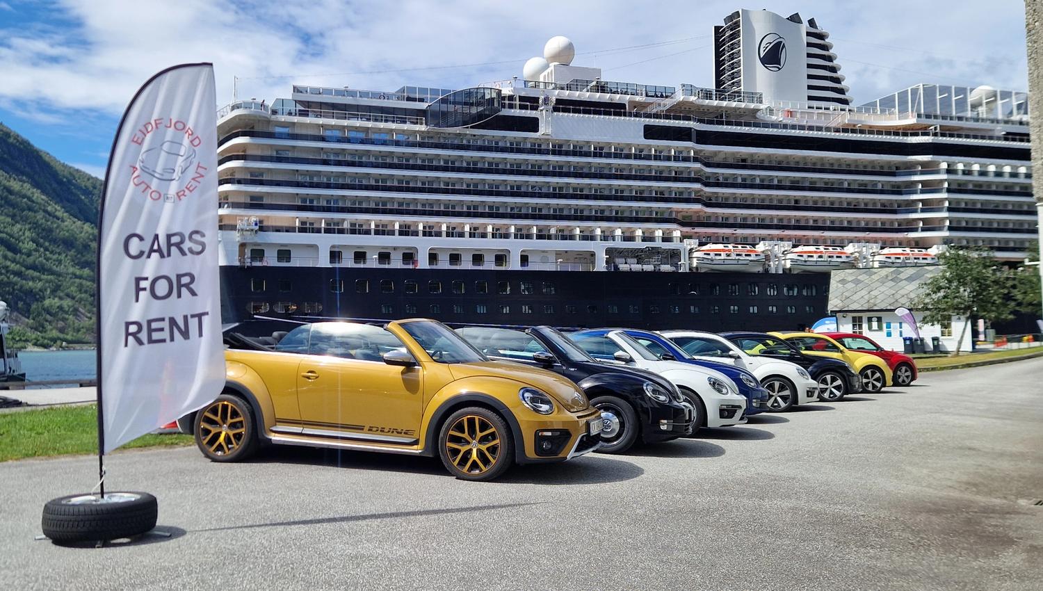 An assortment of VW beetle rental cars in front of a cruise ship.