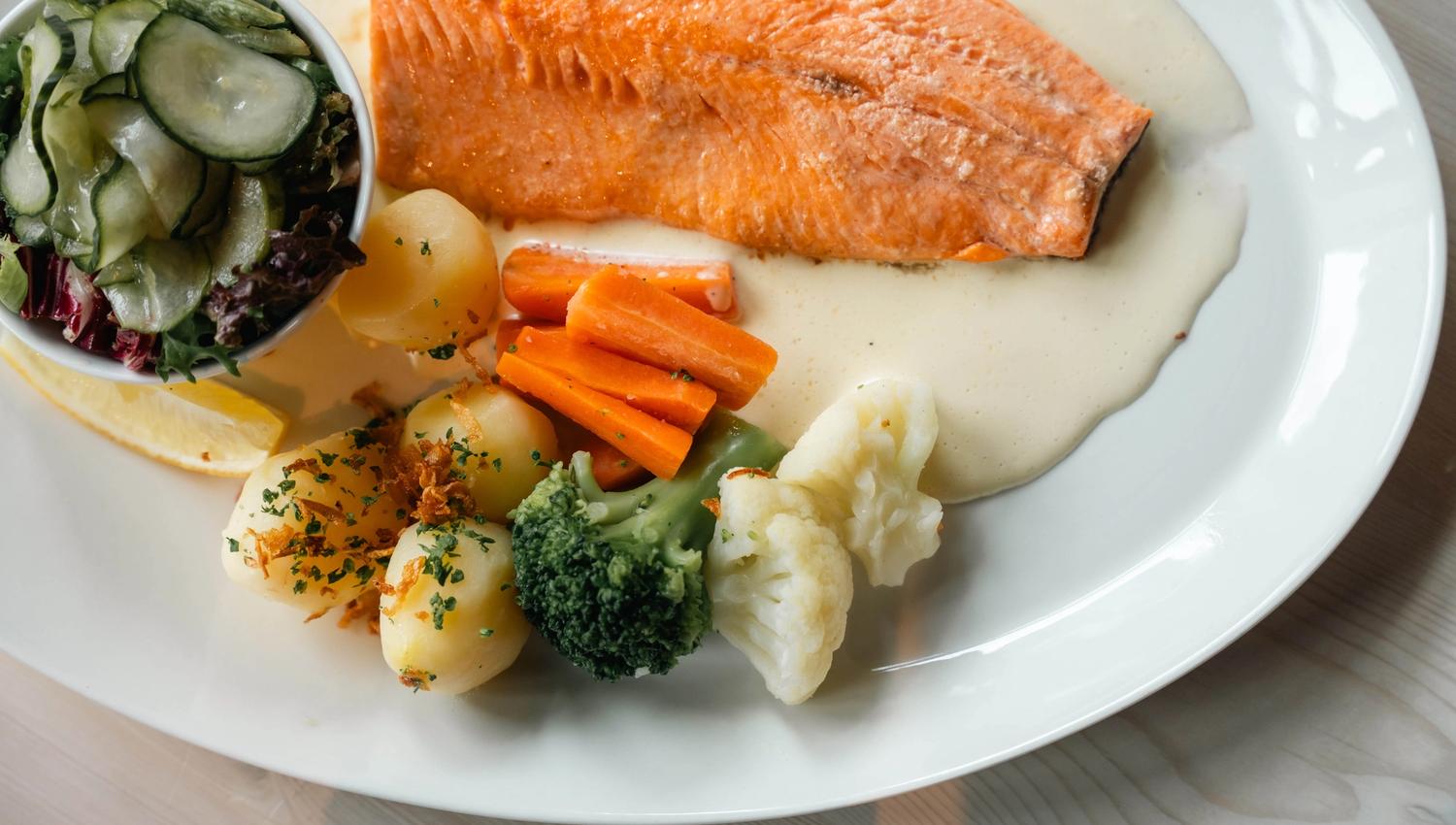 A plate with mountain trout, potatoes, salad and cream sauce.