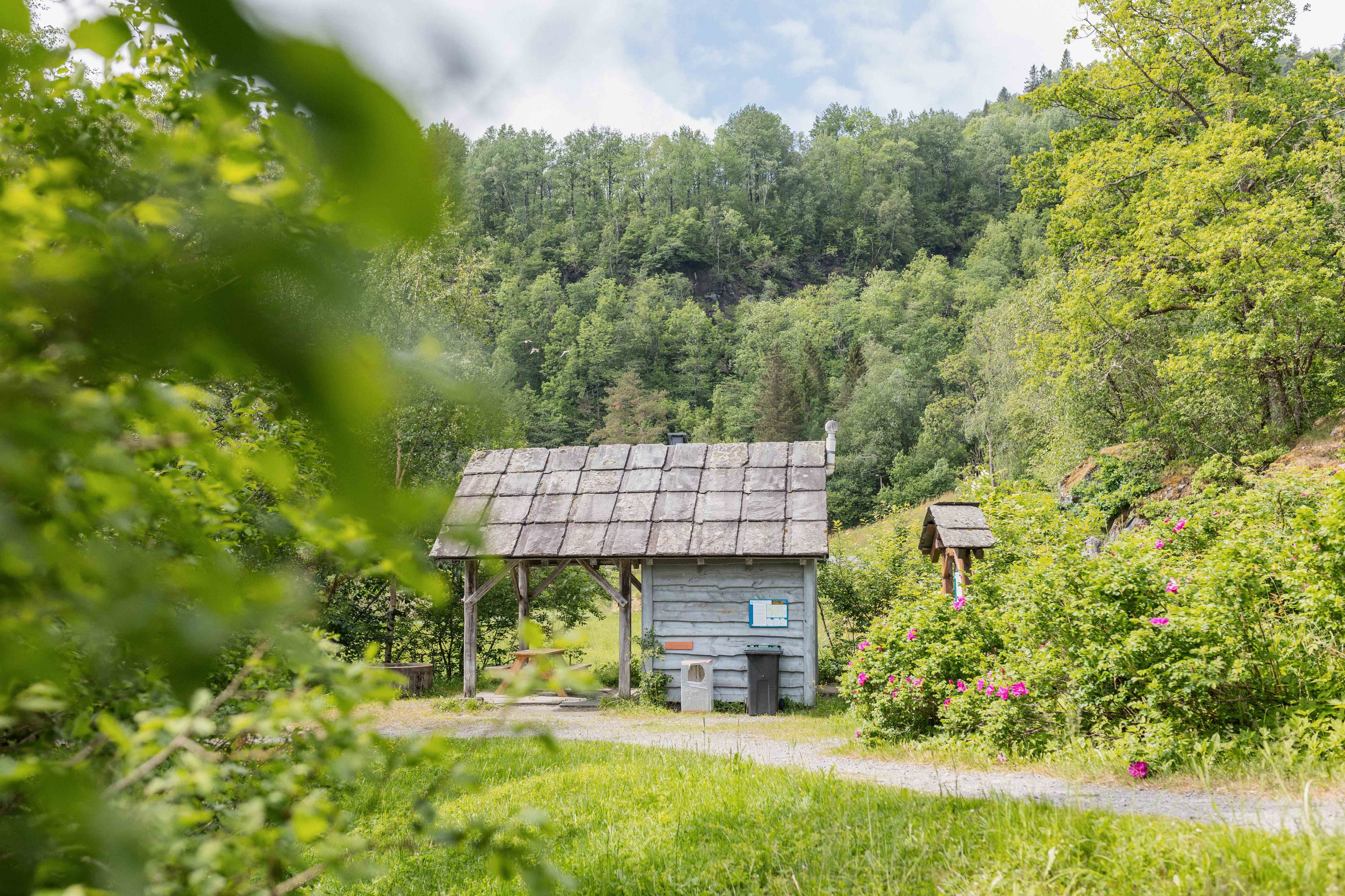 Eit idyllisk lite trebygg ved stien til Gullfiskvatnet, omgitt av grøn natur.