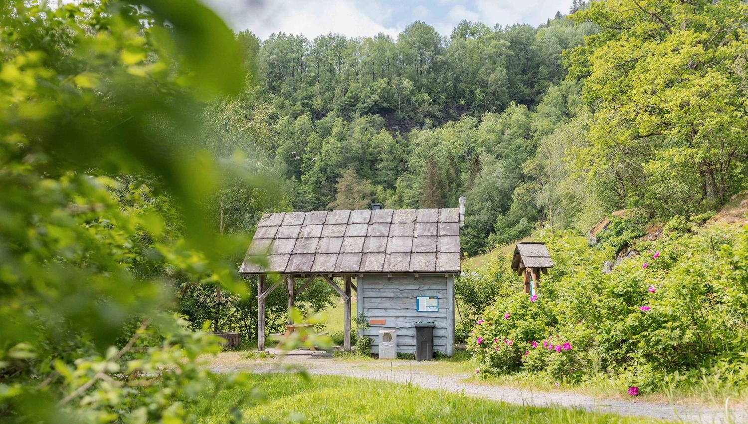 Eit idyllisk lite trebygg ved stien til Gullfiskvatnet, omgitt av grøn natur.