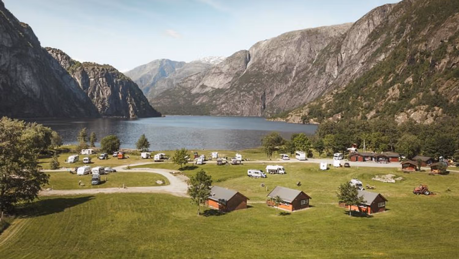 Sæbø Camping von der Hauptstraße aus gesehen, mit dem See und den Bergen im Hintergrund.