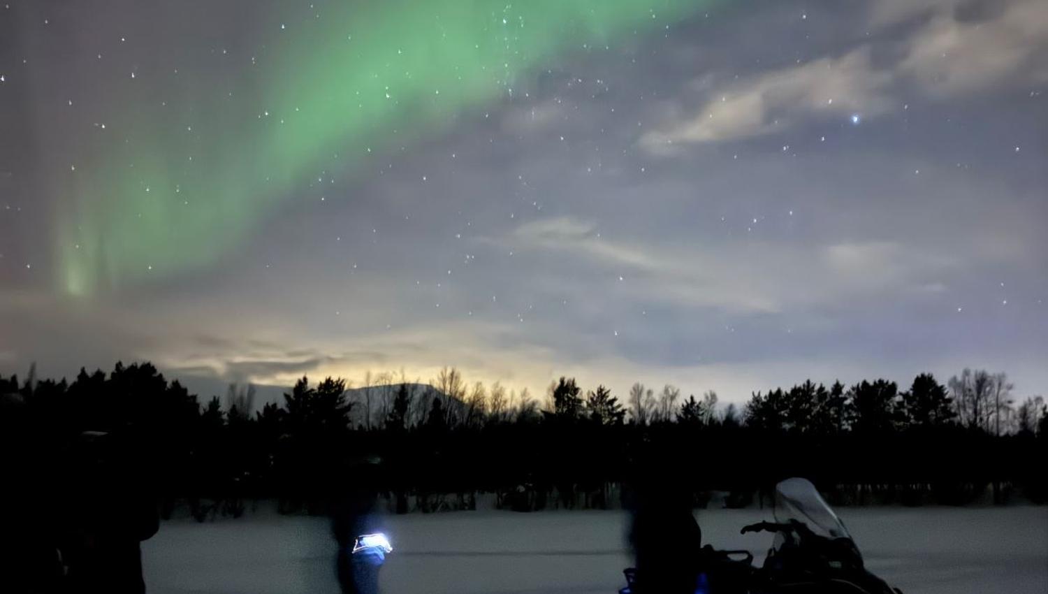Guests with snowmobiles under the Northern Lights in Skibotn Valley