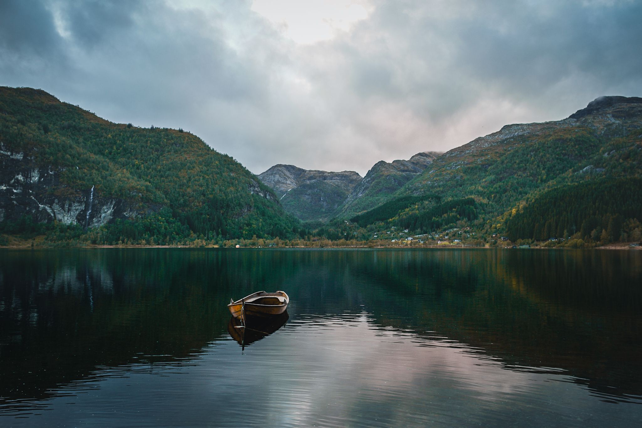 Small wooden boat on calm water surrounded by forested mountains in Hardanger.