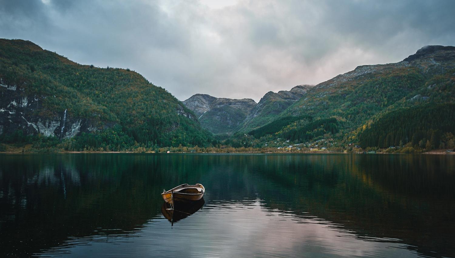 Small wooden boat on calm water surrounded by forested mountains in Hardanger.