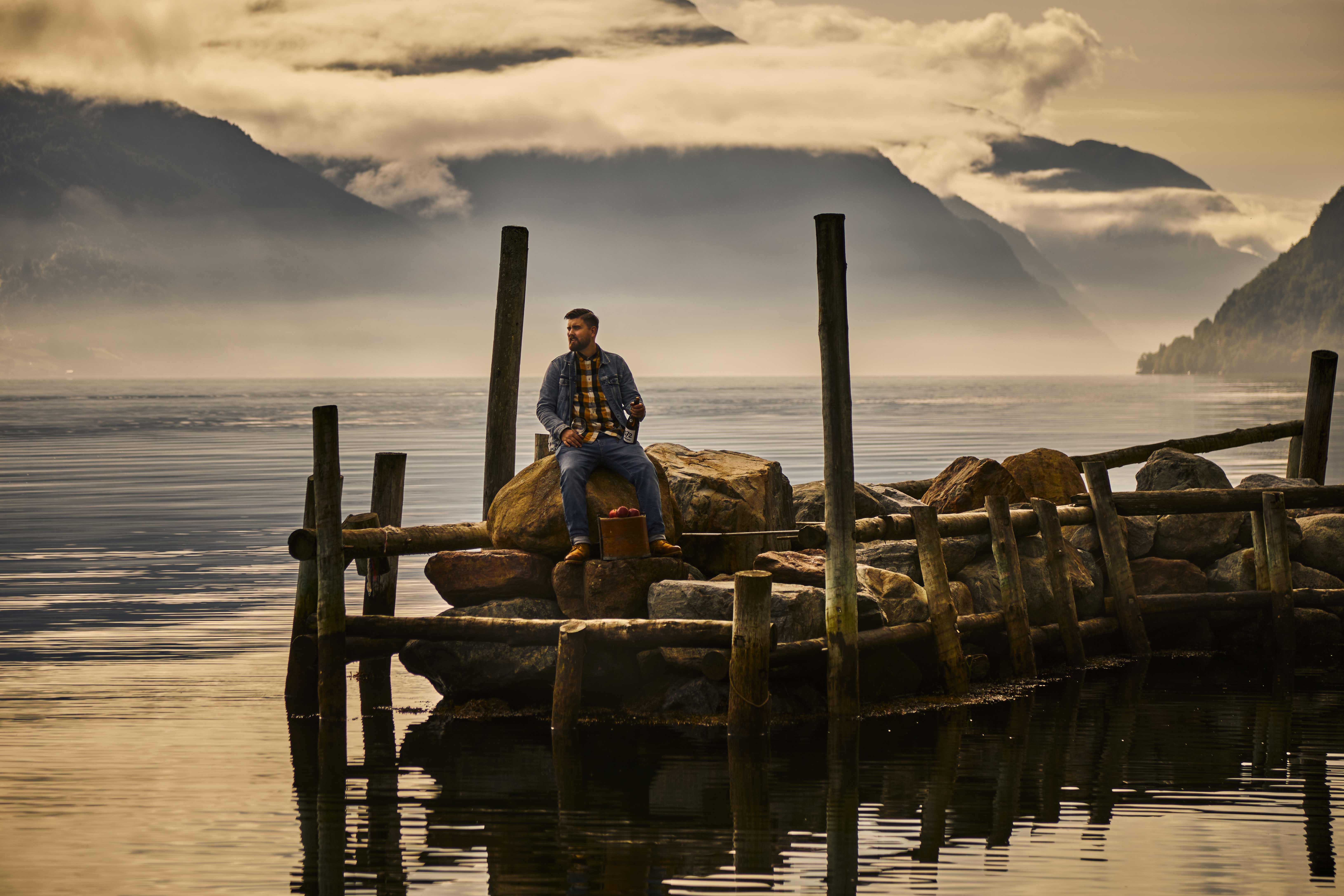 Man sitting on a dock with a bottle of cider by the Sørfjorden in Hardanger.