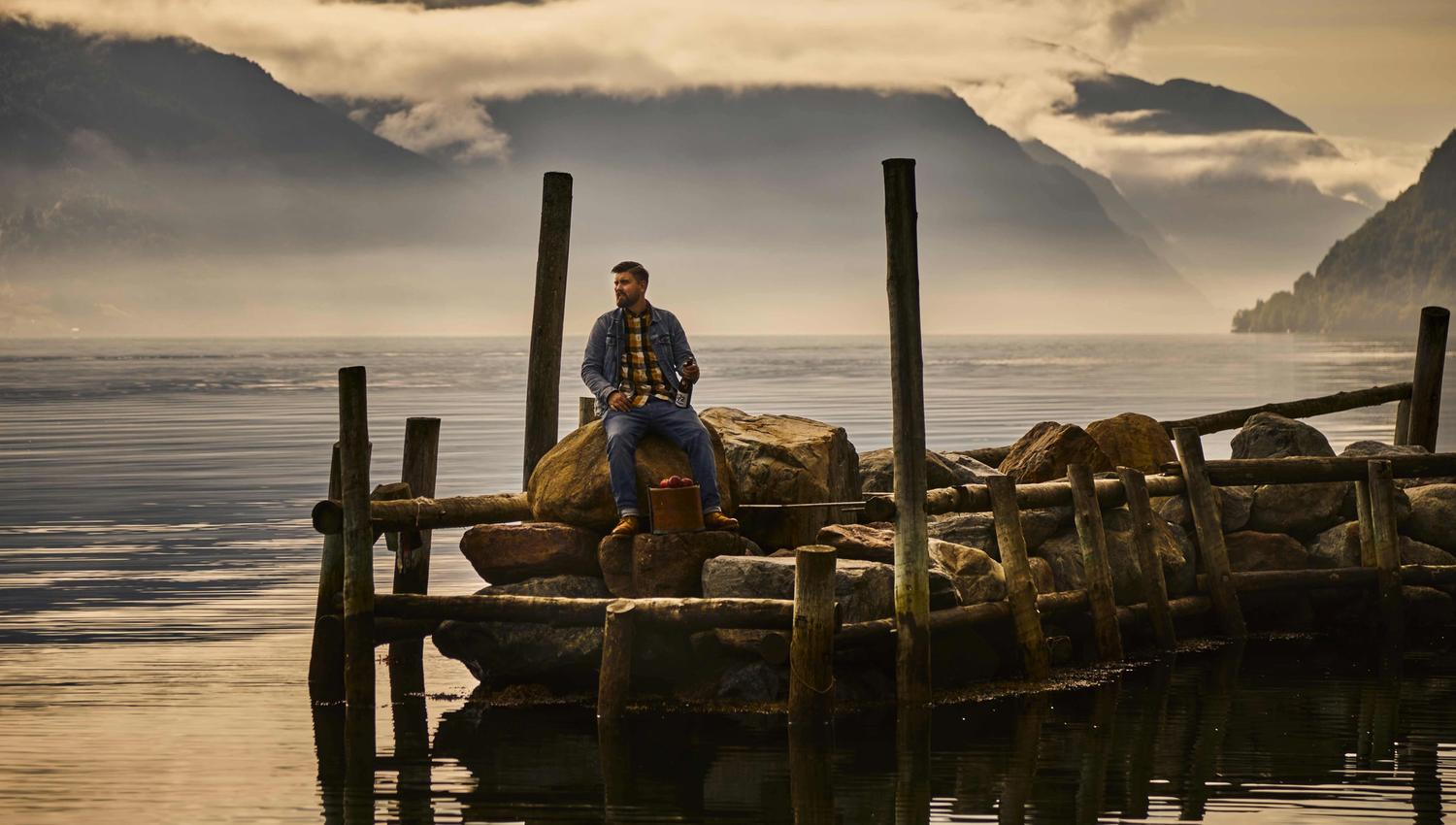 Man sitting on a dock with a bottle of cider by the Sørfjorden in Hardanger.