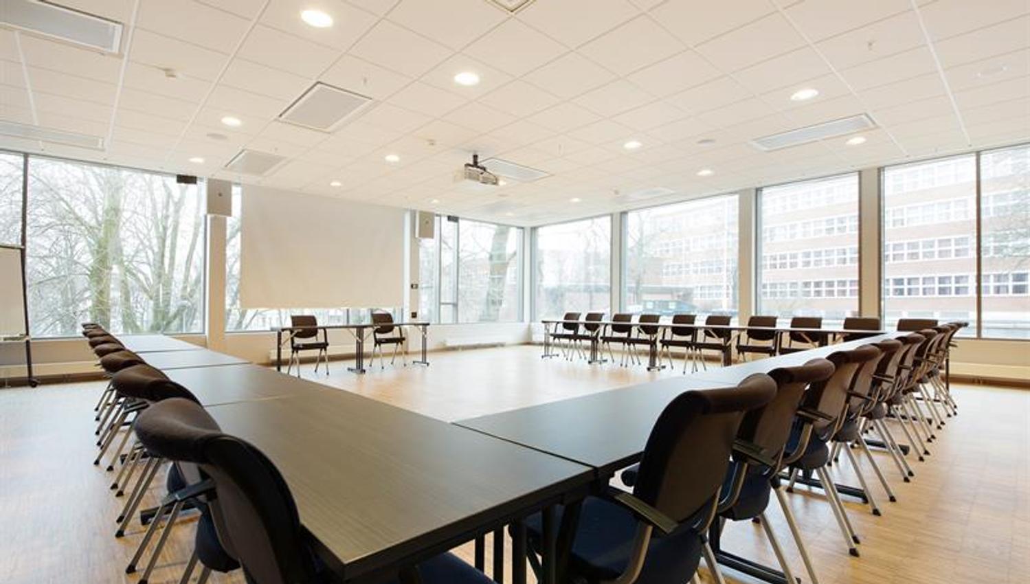 bright and large conference hall with tables in horseshoe-setup and conference technology
