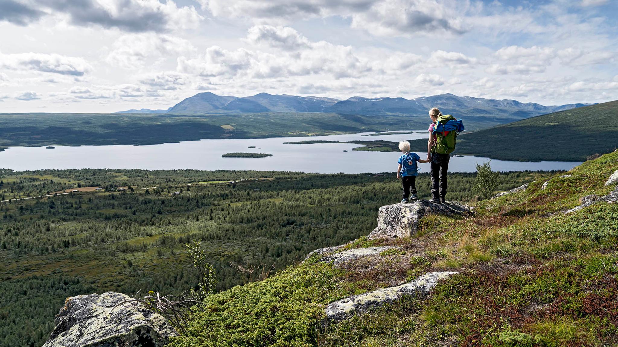 Woman an child standing on a small rock enjoying a magnificent view towards a lake and mountains in the far distance.