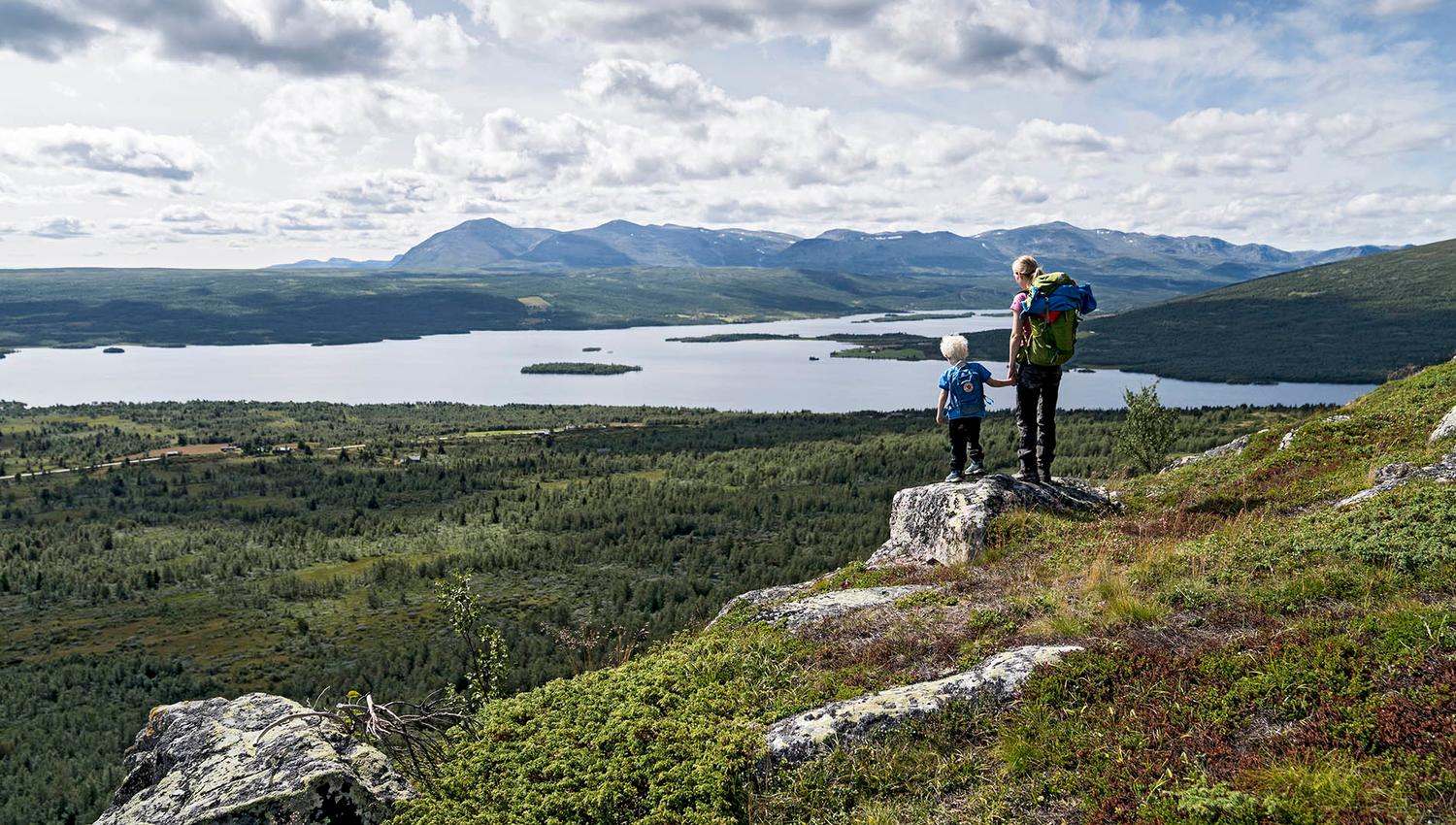 Woman an child standing on a small rock enjoying a magnificent view towards a lake and mountains in the far distance.