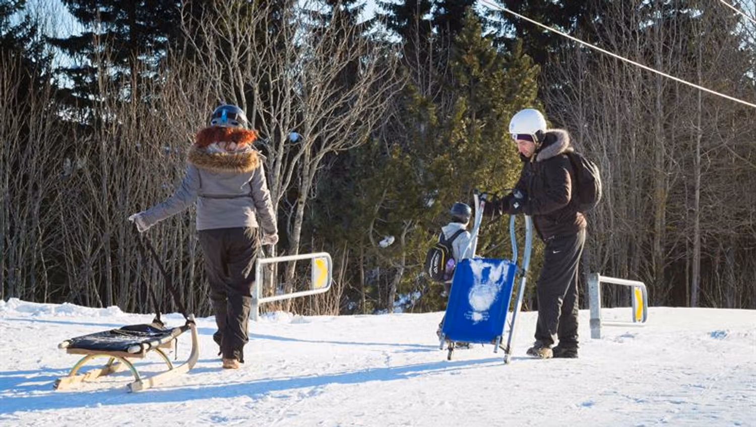 Two people pulling their sleds at the bottom of the hill.