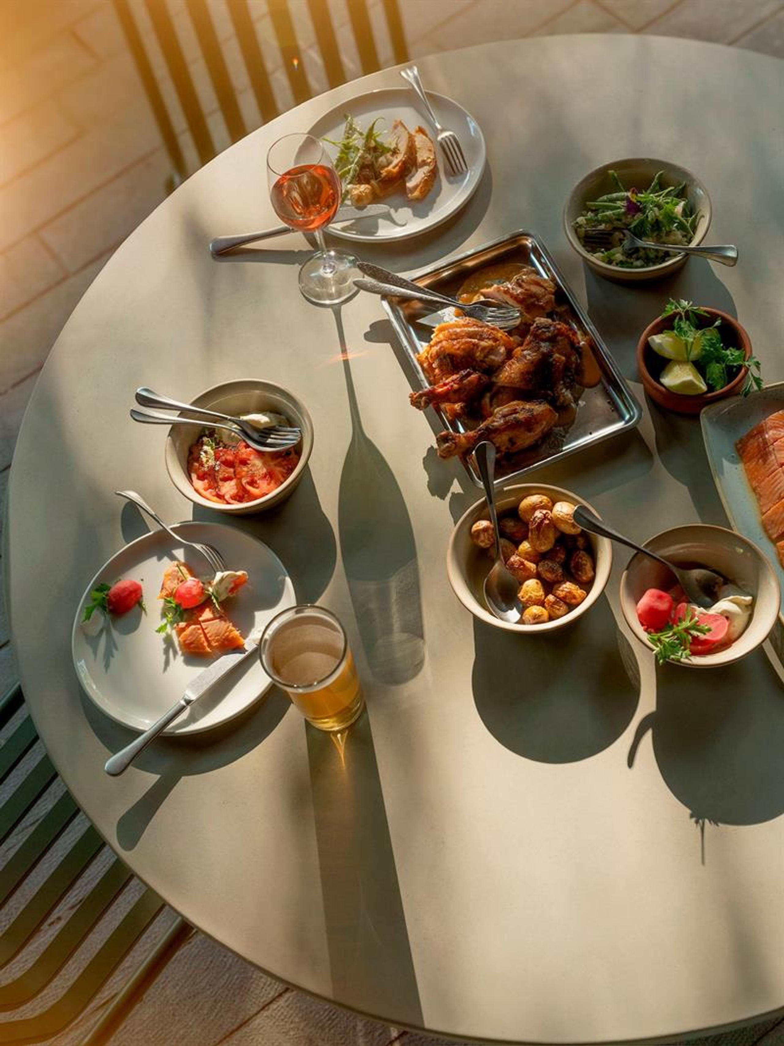 Solfylt bord på terrasse med grillet kylling, småretter, salater og drikke servert til lunsj.