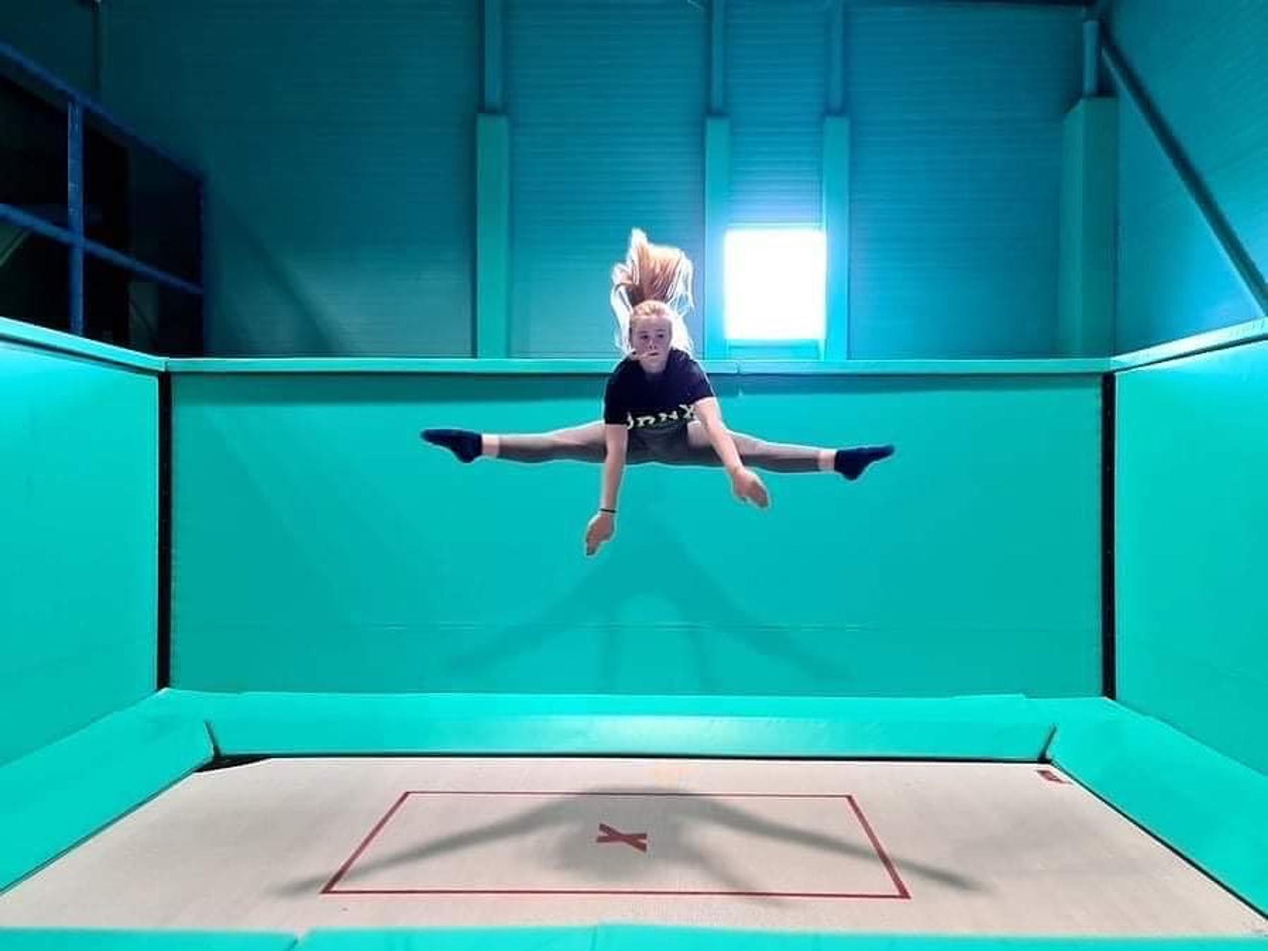 Jente som gjør splitthopp på en trampoline. Foto.
