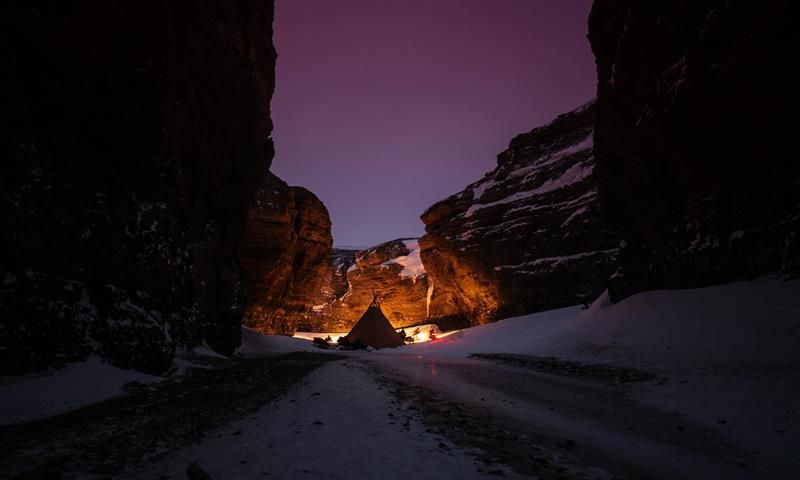 A tent is set up in a narrow valley. The sky is purple.