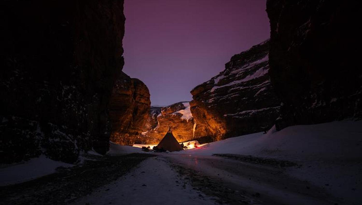 A tent is set up in a narrow valley. The sky is purple.