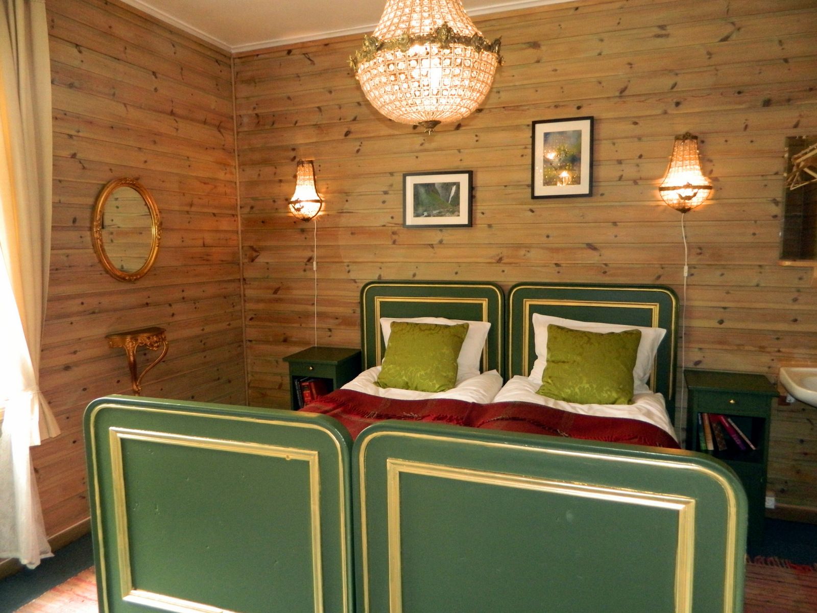 A room with a double bed, green details and a big chandelair hanging above the bed.