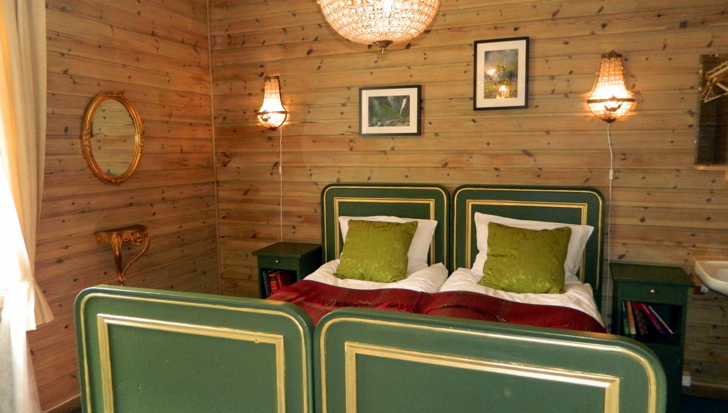 A room with a double bed, green details and a big chandelair hanging above the bed.