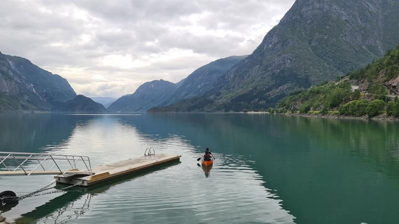 Kayaker near a pier on a calm fjord, surrounded by high mountains in Hardanger.