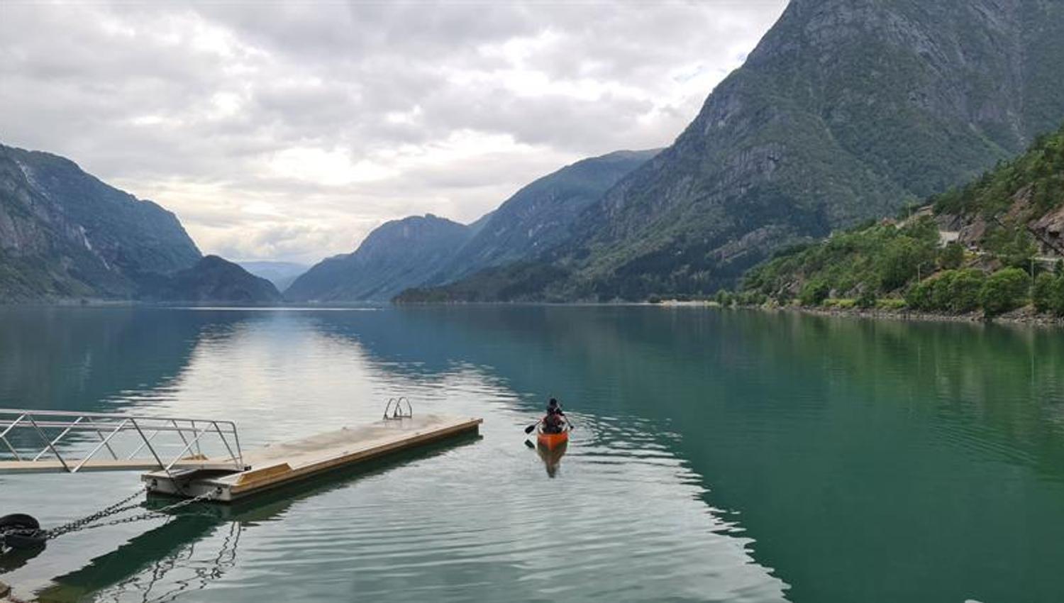 Kayaker near a pier on a calm fjord, surrounded by high mountains in Hardanger.