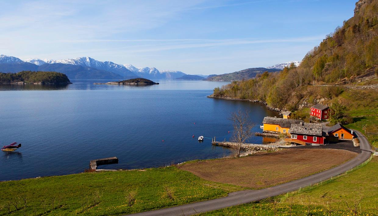 Boathouses by the Hardangerfjord with colorful houses, calm waters, and snow-covered mountains in the distance.