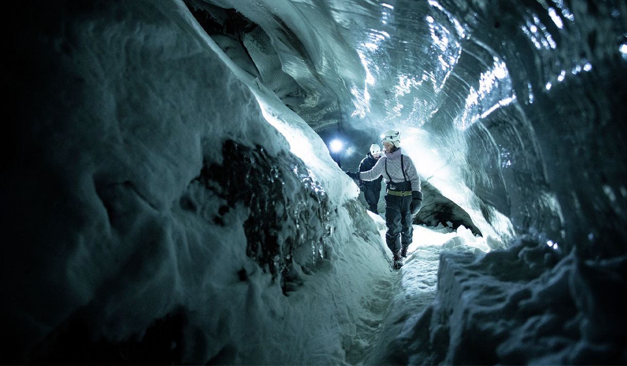 En guide med hjelm og hodelykt på som viser gjester vei gjennom en mørk isgrotte