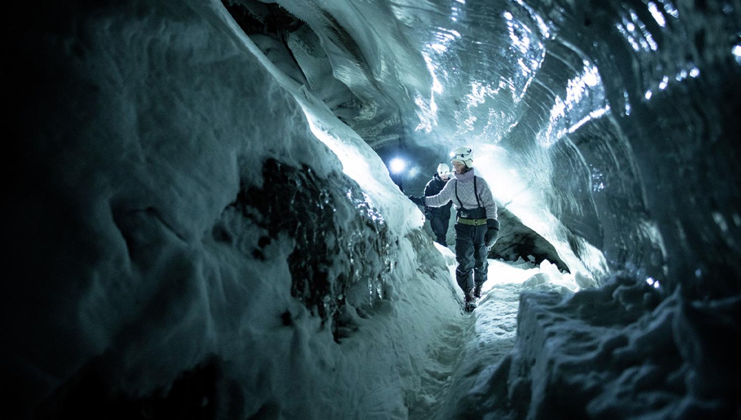 En guide med hjelm og hodelykt på som viser gjester vei gjennom en mørk isgrotte
