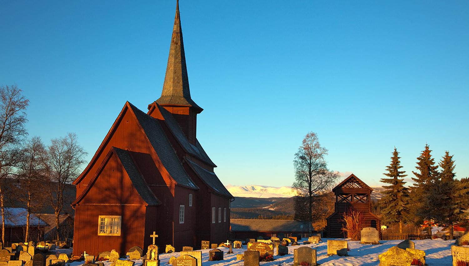 En stavkirke i en snødekt kirkegård i vintersolskinn.