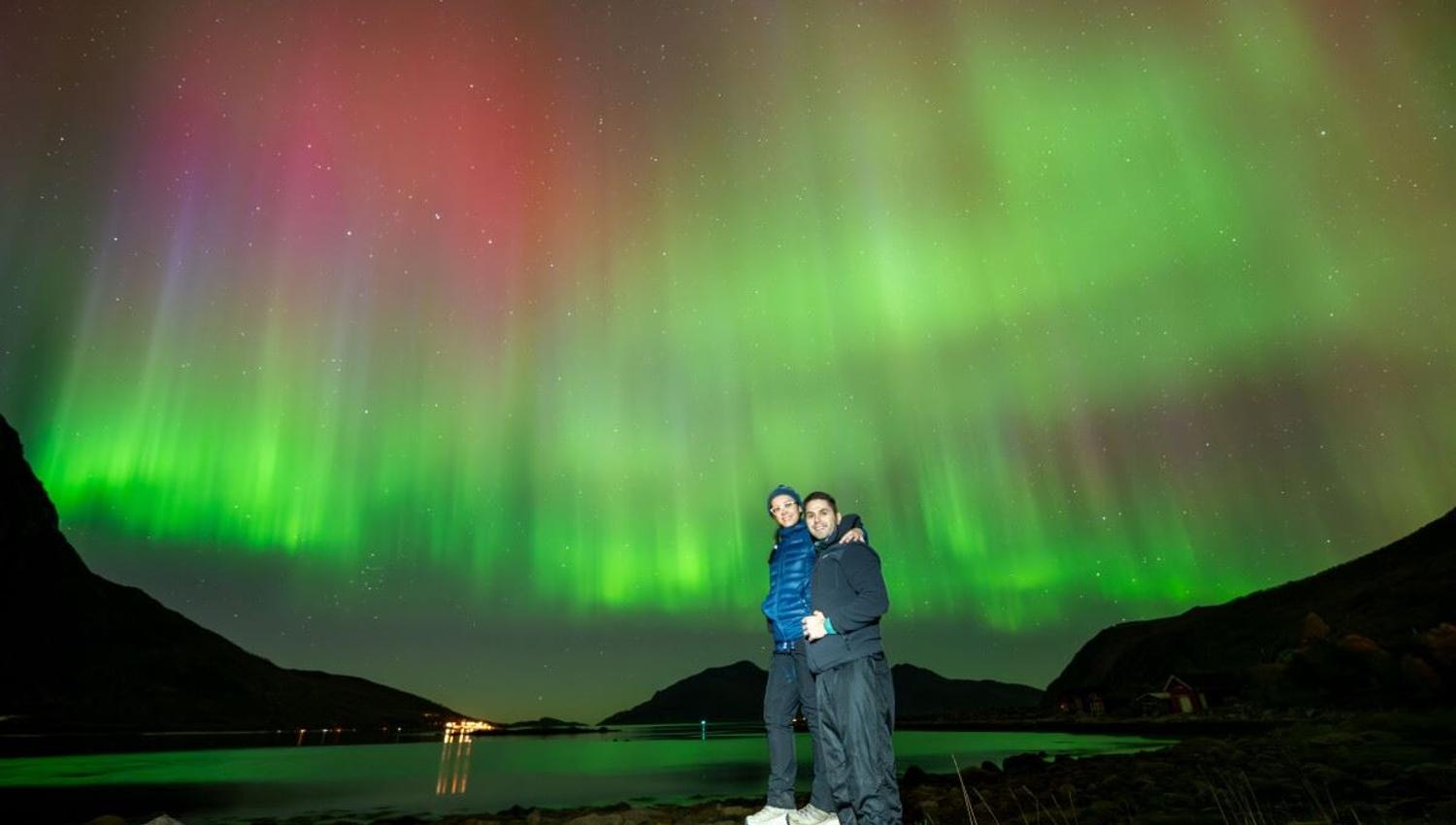Two guests pose in front of an extravagant Northern Lights show