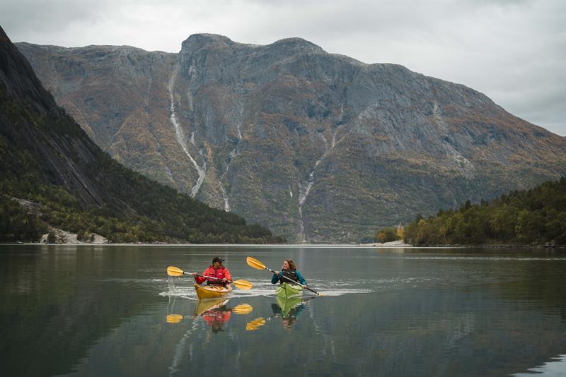 Et par padler kajakk på fjorden med et høyt fjell i bakgrunnen.