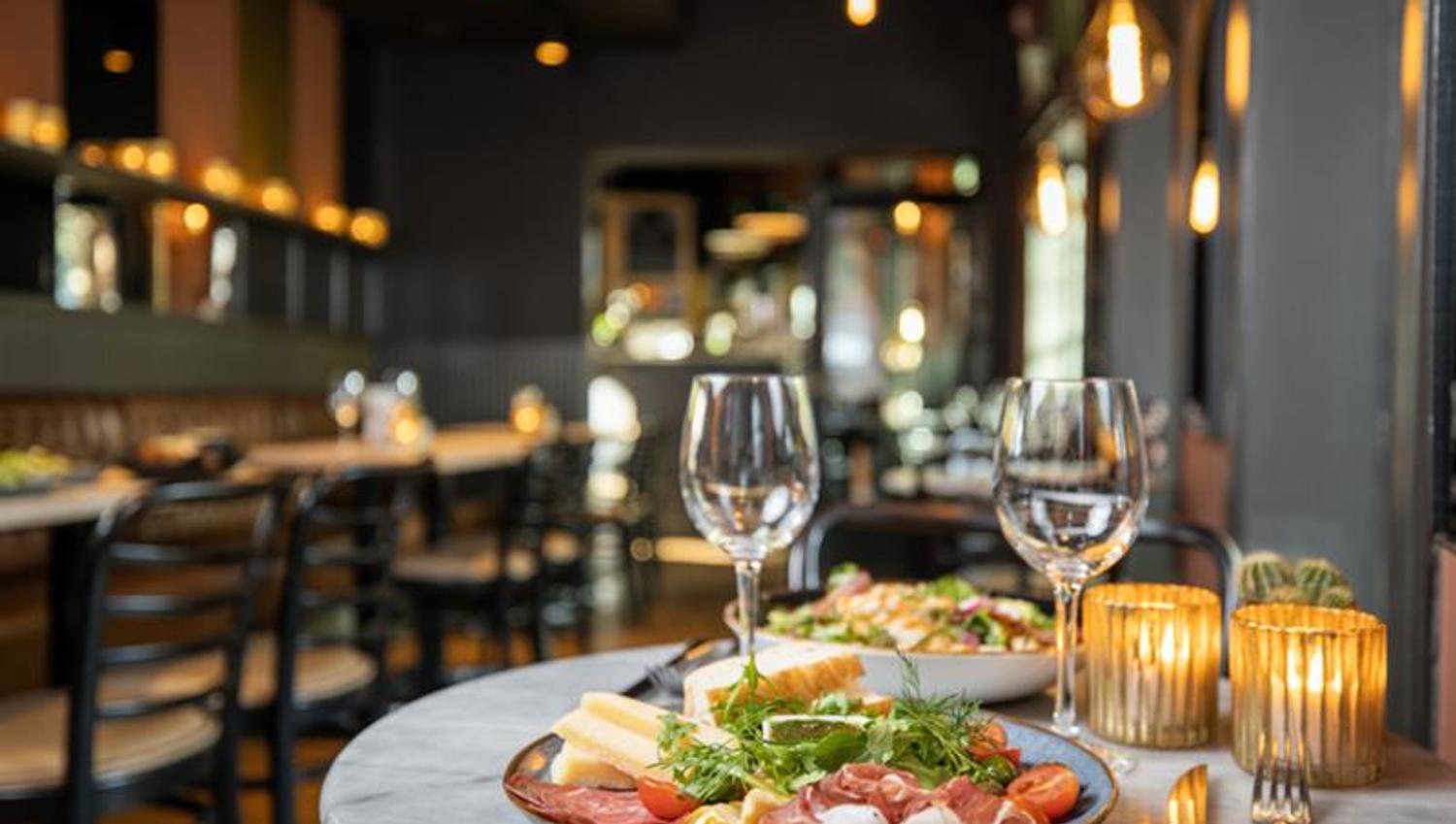 Two plates with food and two wine glasses by a table.