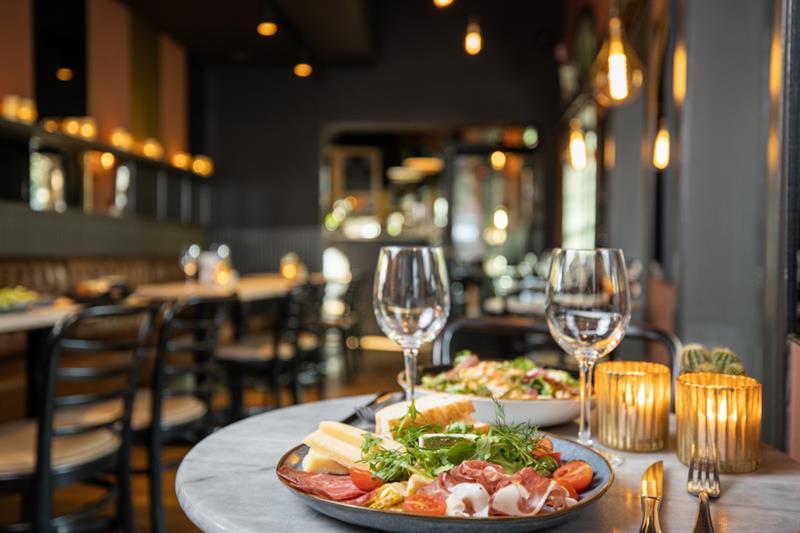 Two plates with food and two wine glasses by a table.