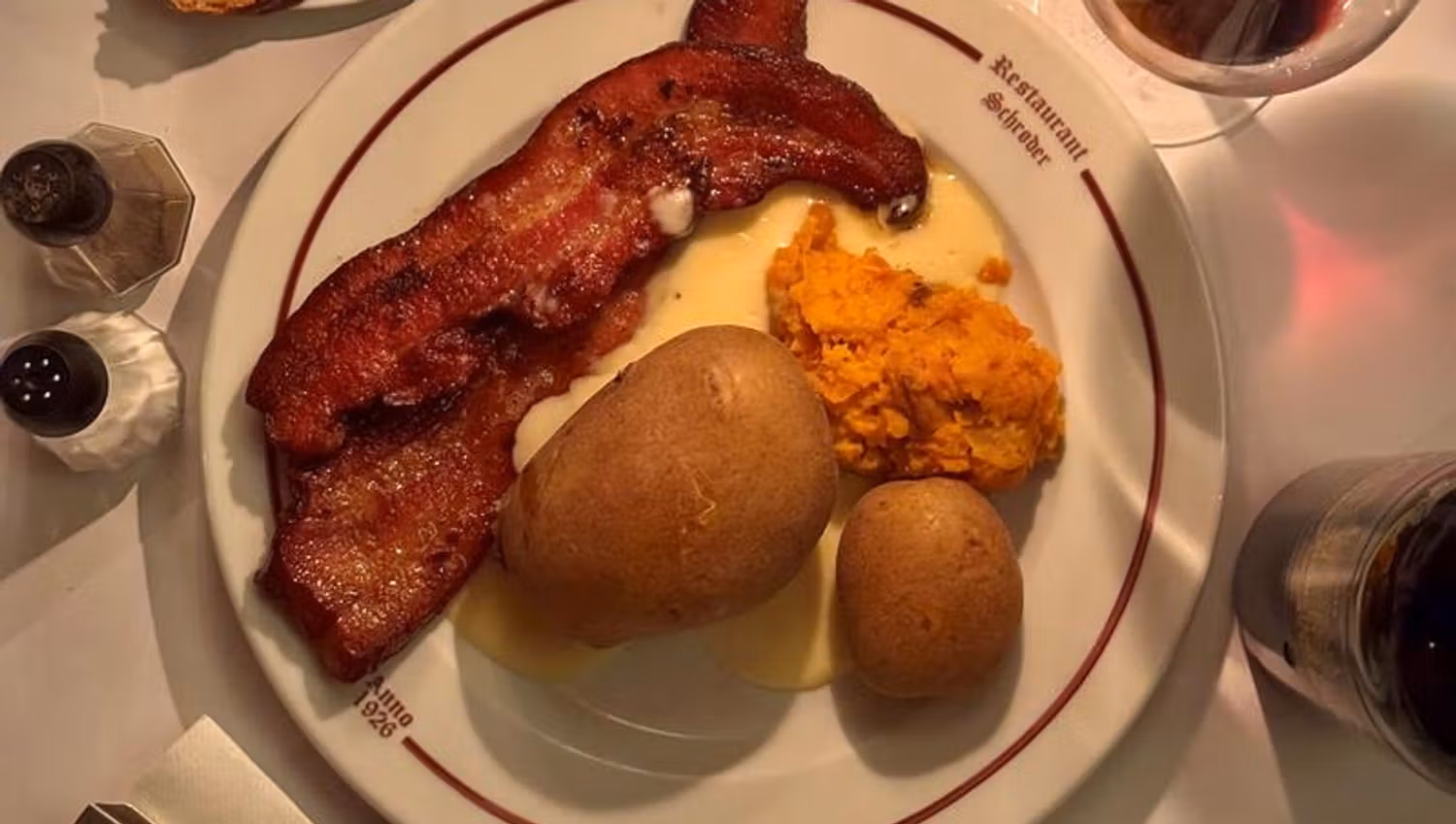 Plate of crispy pork belly, potatoes and root mash served in warm evening light.