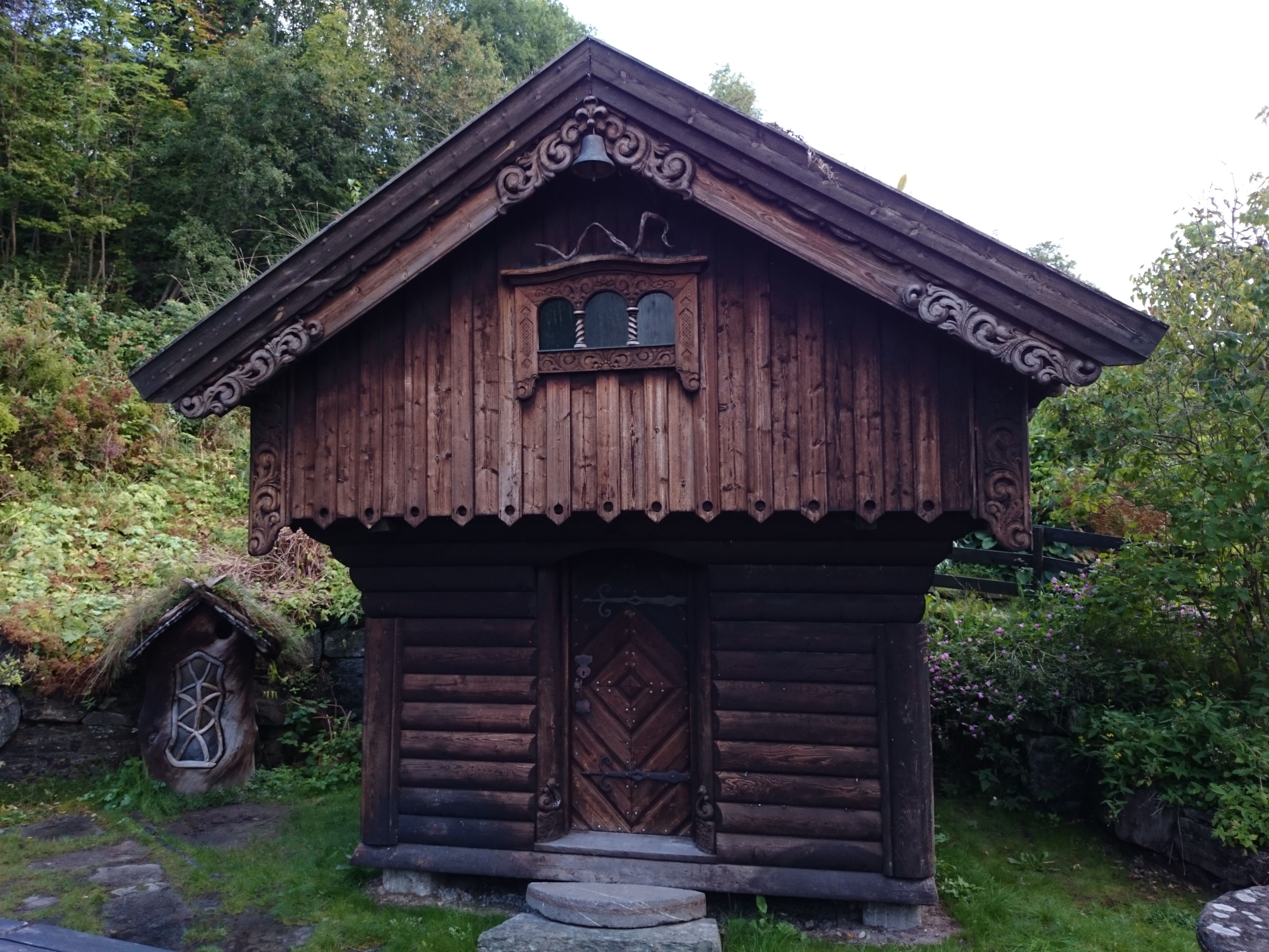 Beautifully carved traditional storehouse in the garden of Ullensvang Gjesteheim, surrounded by lush greenery.