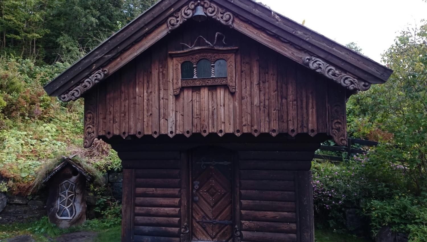 Beautifully carved traditional storehouse in the garden of Ullensvang Gjesteheim, surrounded by lush greenery.