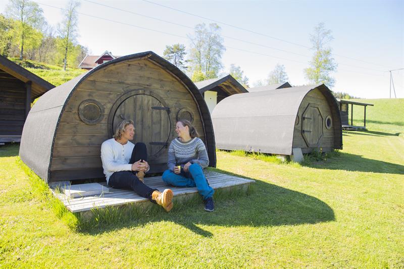 A couple sitting in front of one of the hobbit huts at Adventure Norway, relaxing in the sunshine.