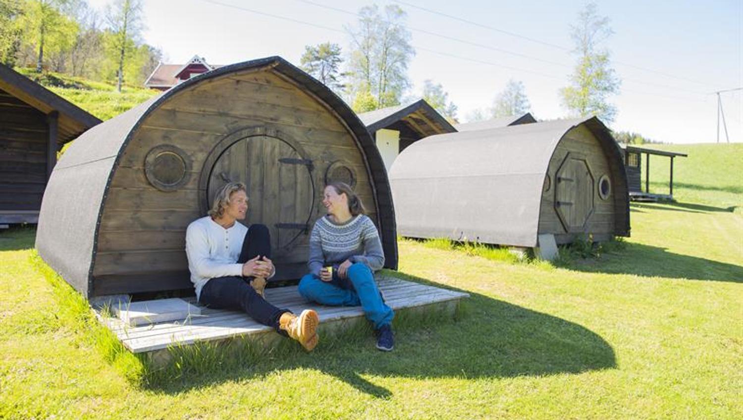 A couple sitting in front of one of the hobbit huts at Adventure Norway, relaxing in the sunshine.